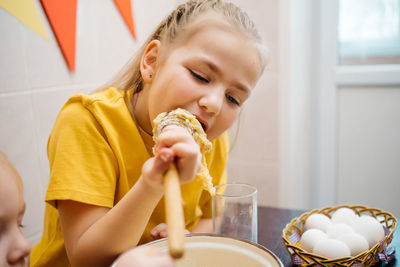 Girl with her brother cooks and tastes dough, white eggs on the table, easter holiday