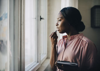 Creative businesswoman talking through earphones while standing by window in office