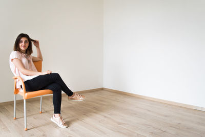 Full length portrait of young woman sitting on chair at home