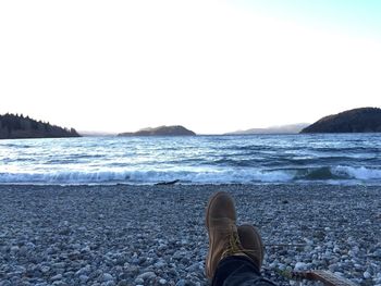 Low section of man standing on beach against clear sky