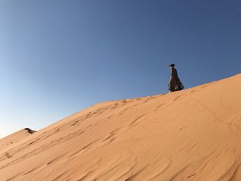 Low angle view of woman walking on sand against clear blue sky