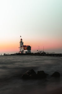 Lighthouse by sea against orange sky