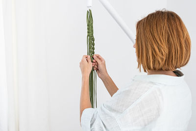 Handmade green macrame plant hangers with potted plant are hanging on woman hand. pot