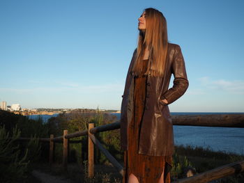 Full length of young woman standing on rock against sky