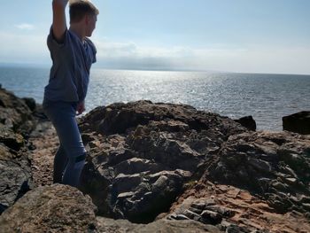 Full length of man on rock at beach against sky