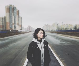 Young woman standing on road in city against clear sky