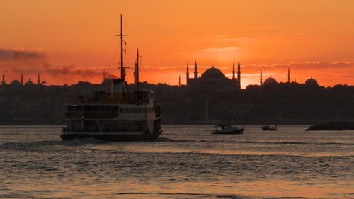 Sailboats in sea against orange sky