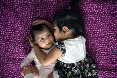 Directly above shot of girl embracing brother while lying on purple blanket