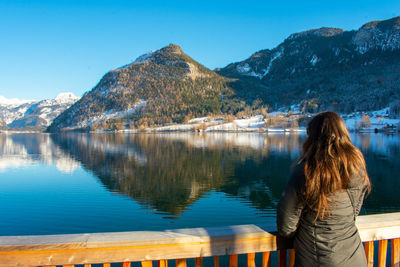 Rear view of woman looking at lake against mountains while standing by railing