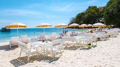 Deck chairs and lounge chair at beach against sky