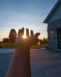 Person hand against built structure at sunset