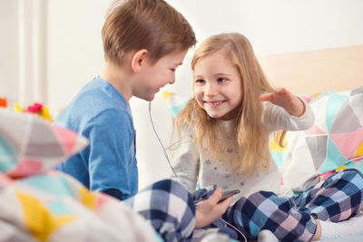 Boy with sister using phone on bed at home