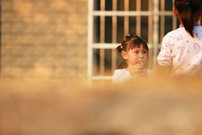 Cute girl drinking drink while looking at sister