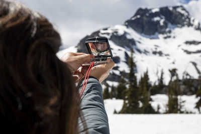 Unrecognizable female hiker using compass for navigation during trip through snowy mountains on cloudy day