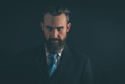 Portrait of serious businessman standing against black background