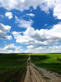 Empty road amidst field against sky