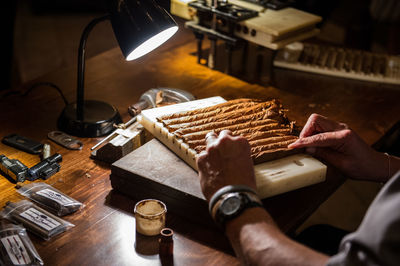 Cropped hands of man rolling cigars on table