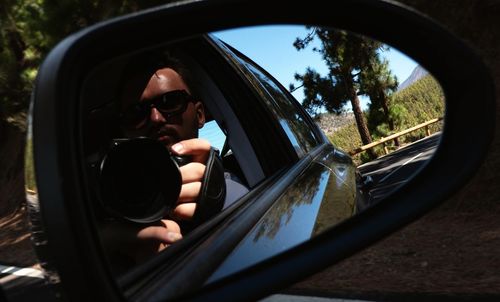 Reflection of man photographing on side-view mirror of car