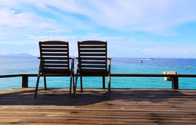 Deck chairs on shore against sky