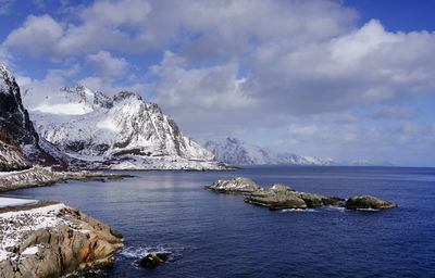 Scenic view of sea by snowcapped mountains against sky