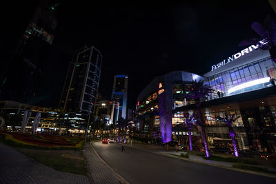 Illuminated street amidst buildings against sky at night