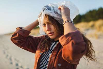 Portrait of young woman with plastic bag standing at beach