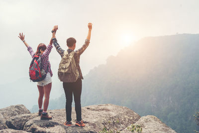 Rear view of man and woman standing on rock against sky