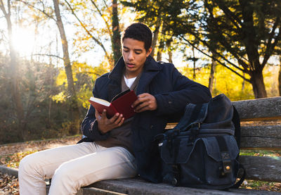 Young man sitting on book against trees