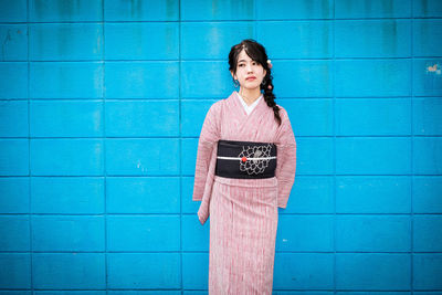 Portrait of a smiling young woman standing against blue wall