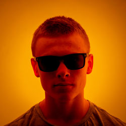 Portrait of boy wearing sunglasses against orange background