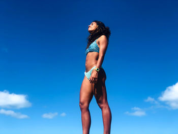 Low angle view of woman in bikini standing against blue sky