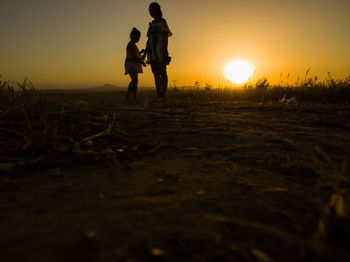 Silhouette people walking on field against sky during sunset
