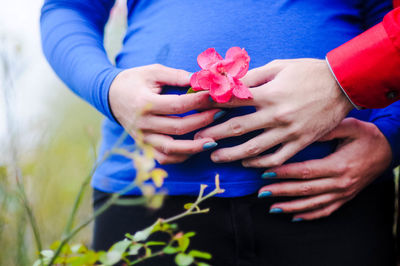 Midsection of man with pregnant woman holding flower on belly 