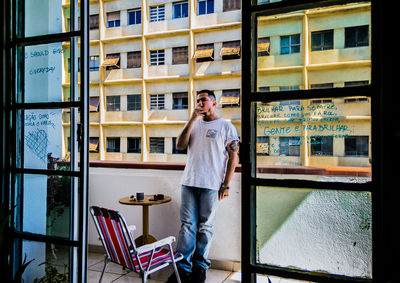 Full length portrait of young man standing against window