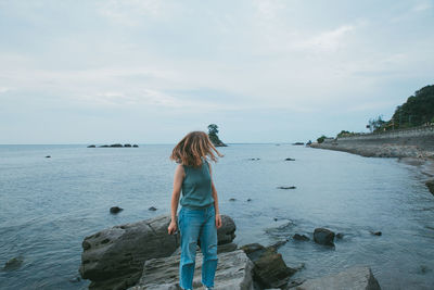 Woman standing on rock by sea against sky