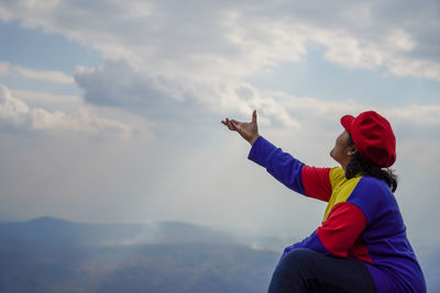 Optical illusion of woman holding clouds while sitting against mountains