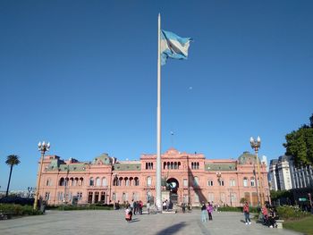 People walking in front of historical building against clear blue sky
