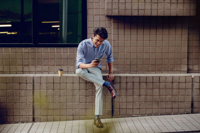 Young man looking away while sitting on wall