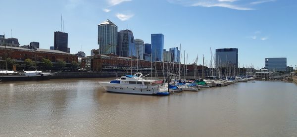 Boats moored in river by buildings against sky in city