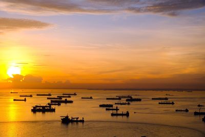 Silhouette boats in sea against orange sky during sunset