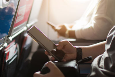 Midsection of passengers using mobile phones while sitting in bus