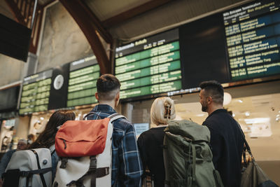 Rear view of family with backpacks looking at arrival departure board at railroad station