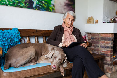 Senior woman using digital tablet with dog sitting on bench at home