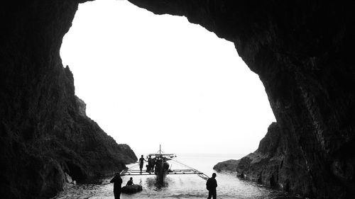 People with outrigger canoe in cave at beach against clear sky