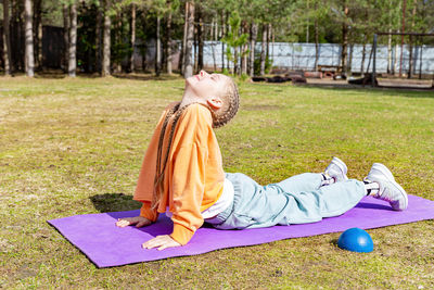 Teenage girl practices yoga in nature on a sunny summer day on a sports mat, stretches. 