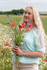 Beautiful middle-aged blonde woman stands among a flowering field of poppies