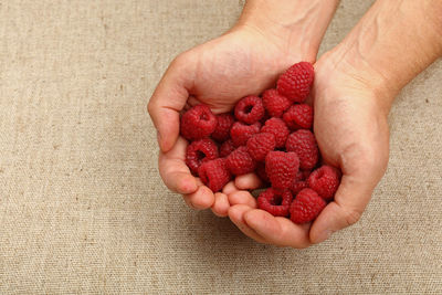 Cropped hands of man holding raspberries over table