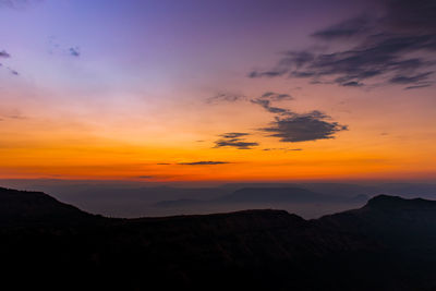 Scenic view of dramatic sky over silhouette mountains during sunset