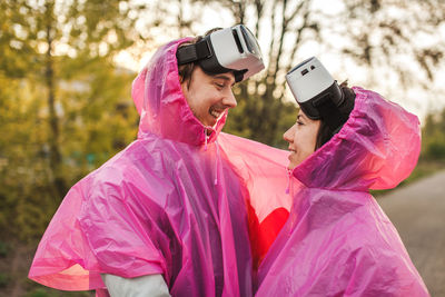 Happy young couple wearing raincoat and virtual reality simulator at park