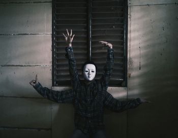 Man wearing mask with artificial hands performing dance against window